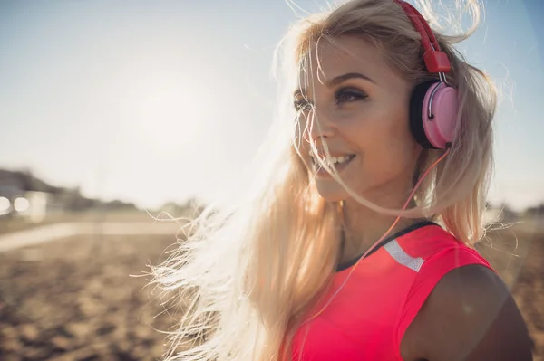 Portrait of young beautiful woman listening to music at beach. Close up face of smiling blonde woman with earphone looking at camera. Girl running at beach and listening to music.