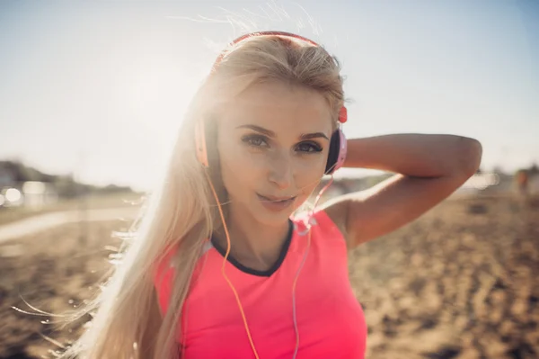 Portret młodej kobiety pięknej, słuchania muzyki na plaży. Bliska twarz uśmiechający się blondynka z słuchawki patrząc na kamery. Dziewczyna, działa na plaży i słuchania muzyki. — Zdjęcie stockowe
