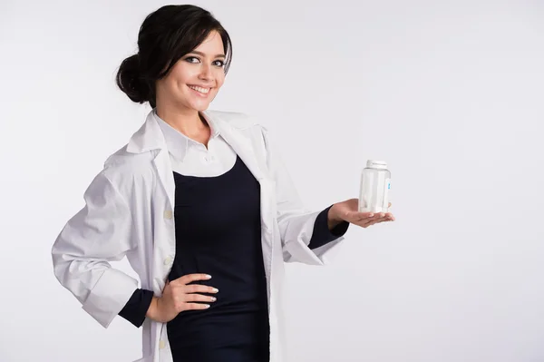 Bella giovane bruna infermiera o medico con gli occhiali in abito blu e camice bianco che tiene una bottiglia di pillole — Foto Stock