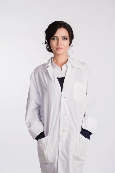 Uśmiechnięta kobieta lekarz medycyny z rękami w kieszeni szaty patrząc na kamery na białym tle — Zdjęcie stockowe