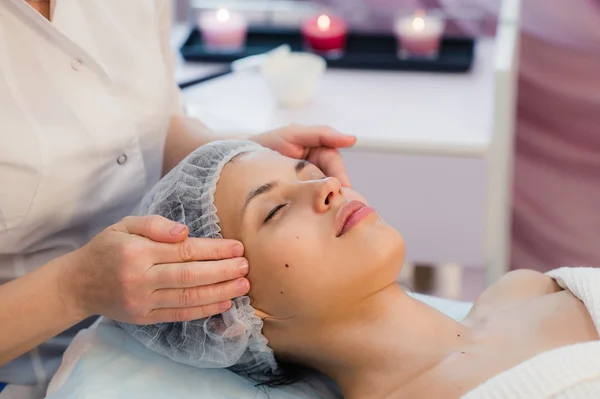 Bella giovane donna sdraiata rilassata in un salone termale e ricevendo massaggio facciale — Foto Stock