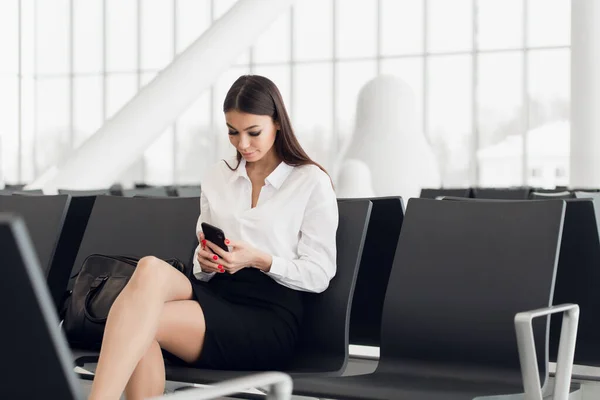 Η κυρία από το αεροδρόμιο περιμένει στο τερματικό. Air ταξιδιωτική έννοια με νέους casual γυναίκα των επιχειρήσεων κάθεται με την ομιλία στο smartphone. — Φωτογραφία Αρχείου