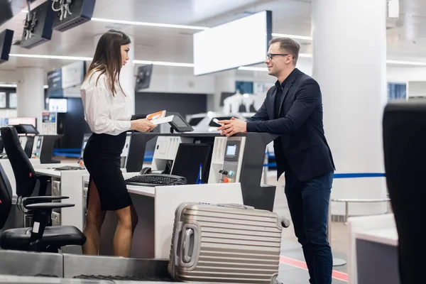 Business trip. Handsome young businessman in suit holding his passport and talking to woman at airline check in counter in the airport