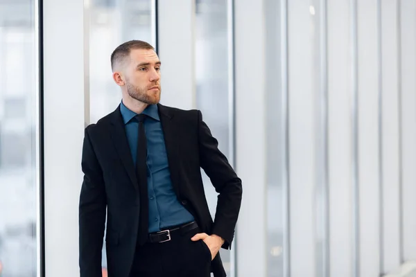 Porträt eines jungen selbstbewussten Geschäftsmannes mit verschränkten Händen am Fenster. — Stockfoto