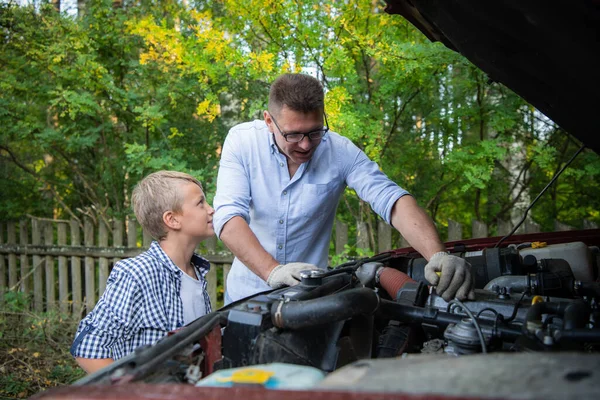 Padre joven enseñando a su hijo a cambiar el aceite de motor en el coche familiar. — Foto de Stock