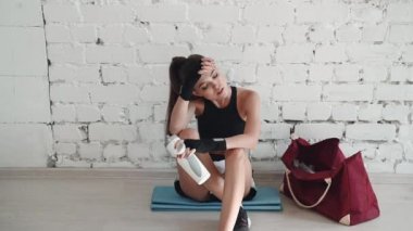 Genç bir kız boks antrenmanı sırasında yoruldu ve dinlenmek ve içmek için duvara yaslandı.