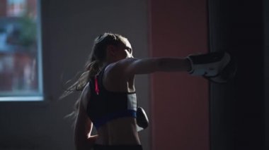 Kickboksçu kızın yavaş hareketi boks salonundaki yarışmalara hazırlanıyor, kum torbasında yumruk tekniği alıştırması yapıyor.
