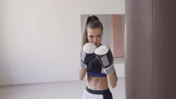 Een strenge trainer kijkt toe hoe zijn vrouwelijke kickbokser student een stomp op een bokszak oefent in een ruime trainingsruimte — Stockvideo