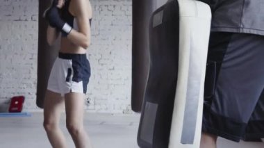 Elinde boks patisi olan kickboks hocasıyla bacak tekmesi pratiği yapan bir kızın yakın çekimi..