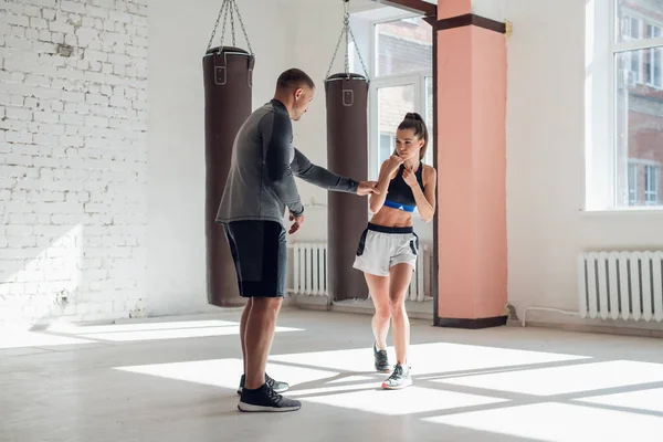 Un giovane pugile attraente insegna alla sua ragazza tecniche di boxe in un loft attrezzato per l'allenamento di boxe — Foto Stock