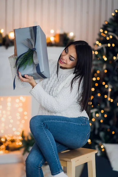 クリスマスツリーと暖炉の前に家に座っているクリスマスプレゼントを開くために興奮した幸せな女性 — ストック写真