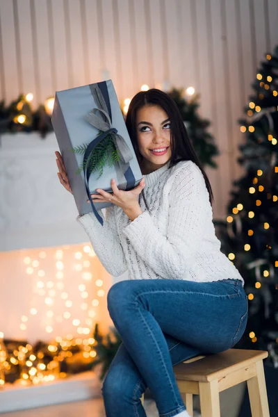 Joyeux jeune femme avec cadeau de Noël surpris et excité assis à la maison contre les décorations de Noël — Photo