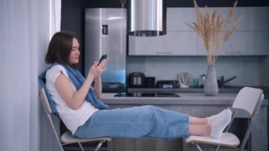 Mutfakta dinlenen bir kadın akıllı telefonu tutar internetten mal seçer, internetten yemek siparişi verir. Modern kablosuz teknoloji hayatı basitleştirir, kolay e-servis kullanımı kavramı.