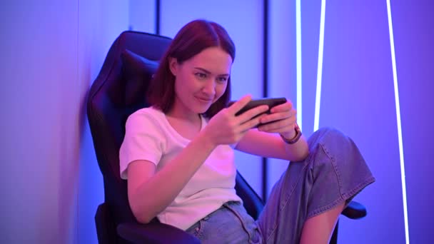 Moskva - Oktober 2020: unga kaukasiska gamer flicka sitta på DxRacer stol och spela online mobilspel med Apple iPhone 11 Pro smarttelefon och med live stream — Stockvideo
