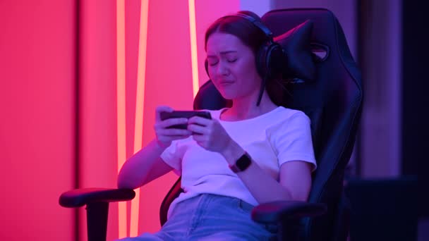 Femme à s'asseoir sur la chaise de jeu joue émotionnellement un jeu vidéo sur un smartphone, perd et se fâche. Images 4K — Video