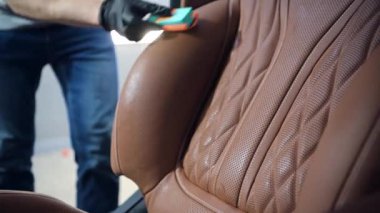 Araba temizleme işçisi özel sünger aplikatörü kullanarak pahalı bir arabanın deri koltuğunu sıvı koruyucu kaplamayla kaplıyor..