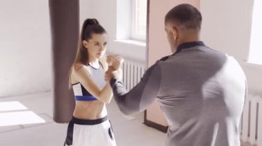 Boks salonunda, deneyimli bir antrenör genç bir kıza doğru duruşu öğretir.