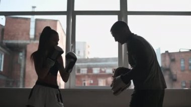 Ellerinde boks patileri olan bir adam hafif spor salonunda acemi bir kıza vurmayı öğretir.