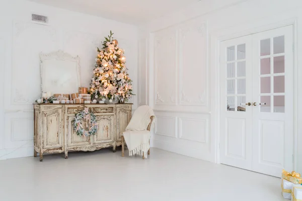 Árbol de Navidad en la cómoda cómoda de madera en el interior blanco, decorado con flores artificiales, guirnaldas y juguetes —  Fotos de Stock