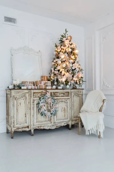 Árbol de Navidad en la cómoda cómoda de madera en el interior blanco, decorado con flores artificiales, guirnaldas y juguetes —  Fotos de Stock