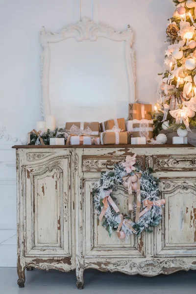 Vánoční stromek na dřevěné truhlici zásuvek prádelník v bílém interiéru, zdobené umělé květiny, girlandy a hračky — Stock fotografie
