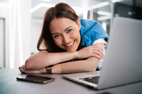 Portret szczęśliwej i czarującej młodej kobiety spędzającej dzień w domu podczas kwarantanny. Uśmiechnięta dziewczyna siedzi przed laptopem i patrzy w kamerę. — Zdjęcie stockowe
