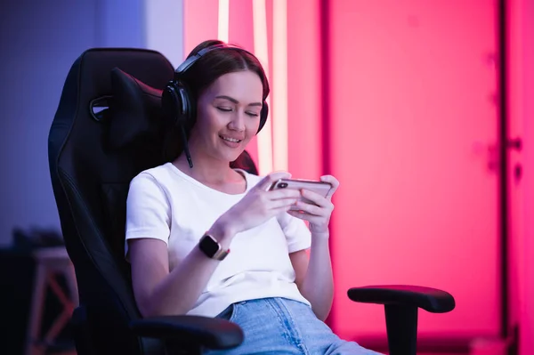 Cep telefonuyla oyun oynayan ve oyun sandalyesinde oturan bir kız. Renkli neon ışıklı oda. — Stok fotoğraf