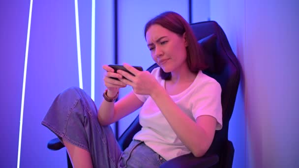 Foto av ung känslomässig och koncentrerad dam gamer sitter inomhus på neon ljus natt spela spel med mobiltelefon. — Stockvideo