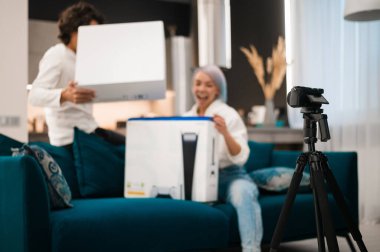 Mutlu video kaydediciler video blogları için paketleri açarken evde yeni bir oyun konsolu ile.