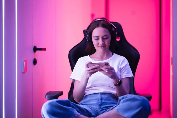 Cybersport-Gamer spielt Handyspiel auf dem Smartphone sitzend auf einem Gaming-Stuhl im neonfarbenen Raum. — Stockfoto