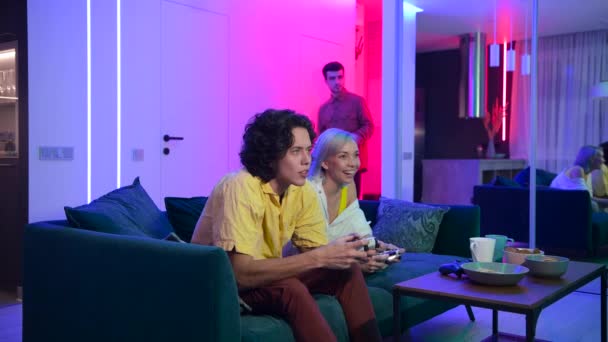 Přítel mladého páru přijde do svého domova hrát hry na herní konzoli na příjemný večer. Šťastní lidé hrají videohry doma. Home party. — Stock video