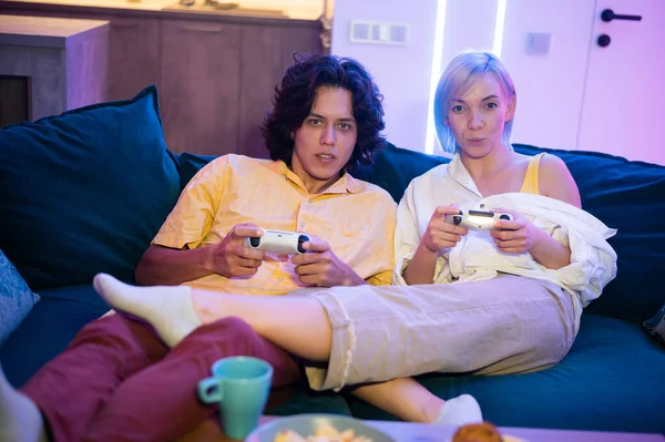 Joven guapo enseñando a jugar los videojuegos a su novia, en el sofá, concepto de entretenimiento en el hogar, videojuegos. — Foto de Stock