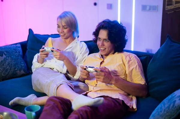 Молодая пара, играющая в видеоигры, сидя на полу в гостиной, освещенном неоновым цветом. — стоковое фото