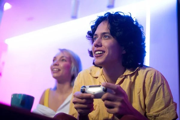 Smiling couple holding gamepads playing video game at home. Low angle shot of young people spending time together during self isolation on pandemic. — Stock Photo, Image