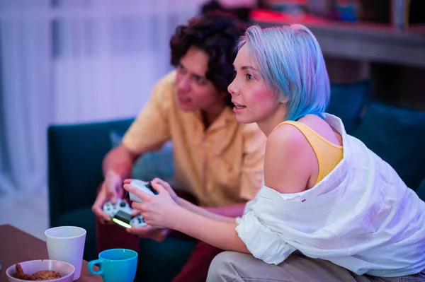 Pareja sonriente sosteniendo mandos jugando videojuegos en casa. Jóvenes que pasan tiempo juntos durante el autoaislamiento ante una pandemia. — Foto de Stock