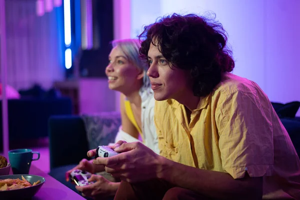 Молодые веселые кавказский муж и жена играют в видеоигры друг против друга дома, наслаждаясь досугом — стоковое фото