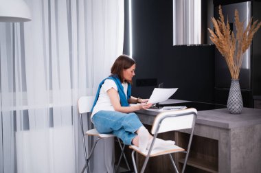 Uzaktan çalışan ya da internetten eğitim alan, dizüstü bilgisayar kullanan, notlar alan, evde oturan bir kadın. Çevrimiçi iş, iş yerinde genç bir profesyonel. Evden çalışmak.