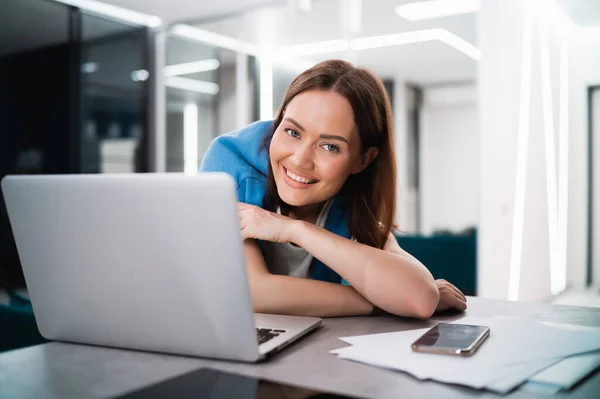 Una joven blogger influencer sonriente que trabaja en casa. Chica feliz trabajando remotamente desde casa sentado en el escritorio con el ordenador portátil y sonriendo a la cámara. — Foto de Stock