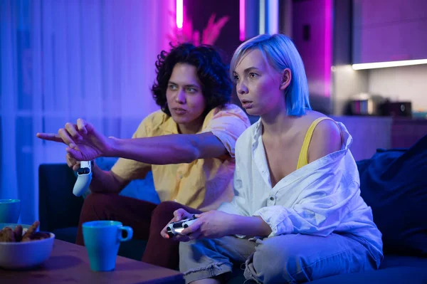 Glückliche junge Leute, die Videospiele auf der Konsole spielen, während sie auf der Couch vor dem Fernseher sitzen. Millennial-Paar verbringt lustige Zeit zusammen zu Hause. Zimmer mit Neonlicht. — Stockfoto