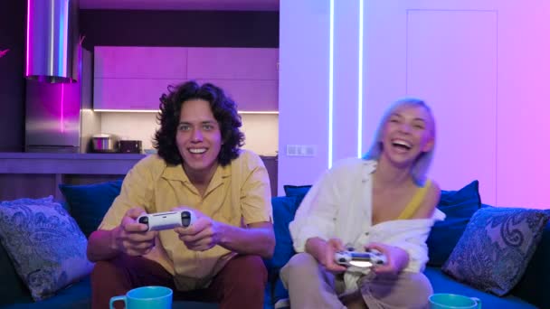 Handsome young man teaching how to play the video games to his girlfriend, on the couch, concept about home entertainment, video games. — Stock Video