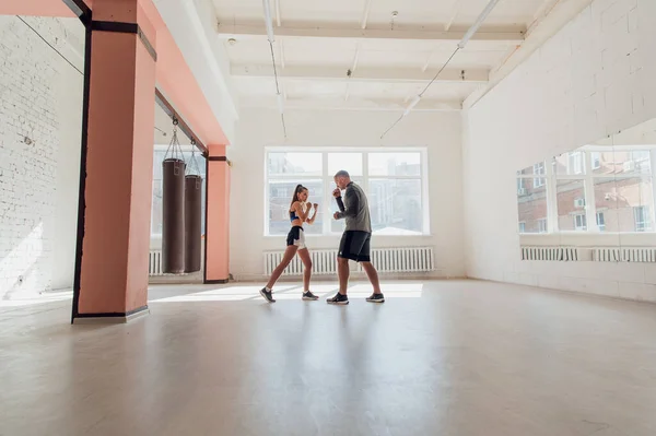 Un allenatore esperto mette la tecnica dei colpi ad una giovane ragazza nella sala da boxe — Foto Stock