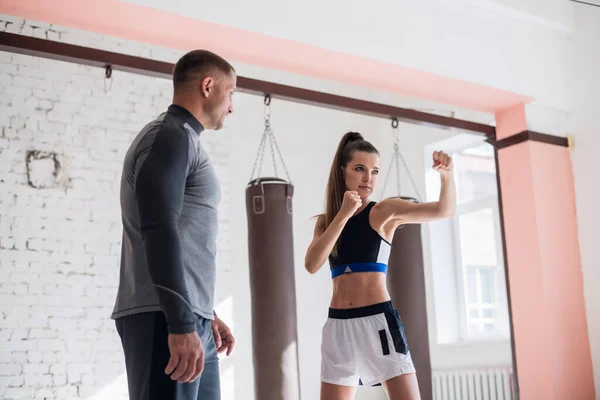 Un giovane pugile attraente insegna alla sua ragazza tecniche di boxe in un loft attrezzato per l'allenamento di boxe — Foto Stock