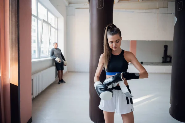 Ritratto con profondità di campo all'interno della sala di formazione. Bella forte pugile femminile e il suo partner sparring maschile sullo sfondo — Foto Stock