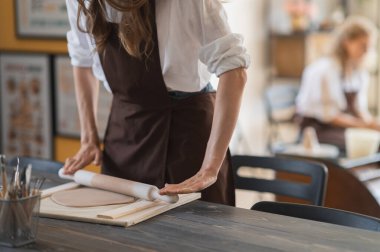 Çömlek kursunda oklavayla çalışan genç bir kadın. Sanatçı, farklı çömlek araçları ile büyük ahşap merdane kullanarak çiğ kil yuvarlar.
