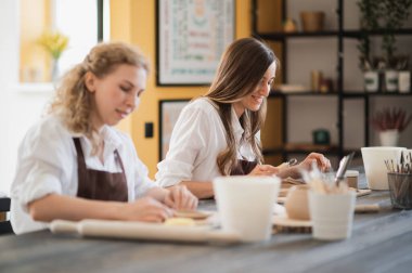 Kadın çömlekçi masadaki kil parçasını şekillendiriyor. Kadın seramik bir şey yapıyor. Sanat stüdyosunda çömlekçilik, el yapımı ve yaratıcı beceriler..