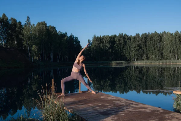 Beautiful young woman performing a spiritual yoga pose on a forest lake at sunny day, sunrise zen wellness — Stock Photo, Image