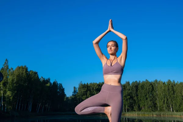 Chica haciendo yoga árbol pose en la naturaleza. Postura de yoga de chica. Deportes al aire libre que se extienden en un lago forestal. — Foto de Stock