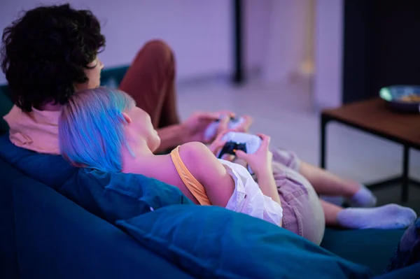 Pareja sonriente sosteniendo mandos jugando videojuegos en casa. Jóvenes que pasan tiempo juntos durante el autoaislamiento ante una pandemia. Fotos de stock libres de derechos