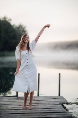 Beyaz elbiseli mutlu kadın gölde sabahtan zevk alıyor. Sis suyun üzerinde yüzüyor..