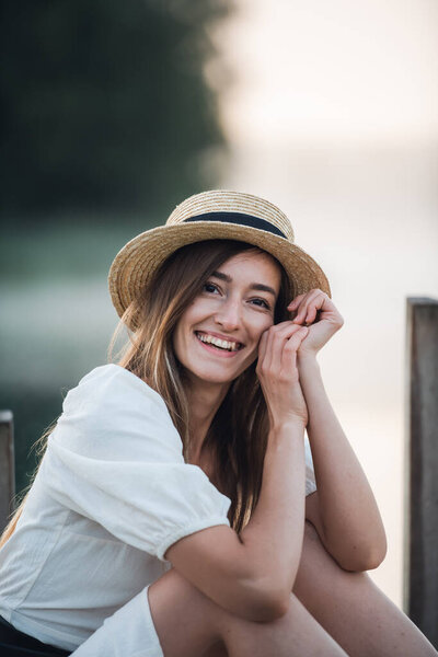 Portrait of a happy caucasian woman in a white dress and hat outdoors sitting and smiling.